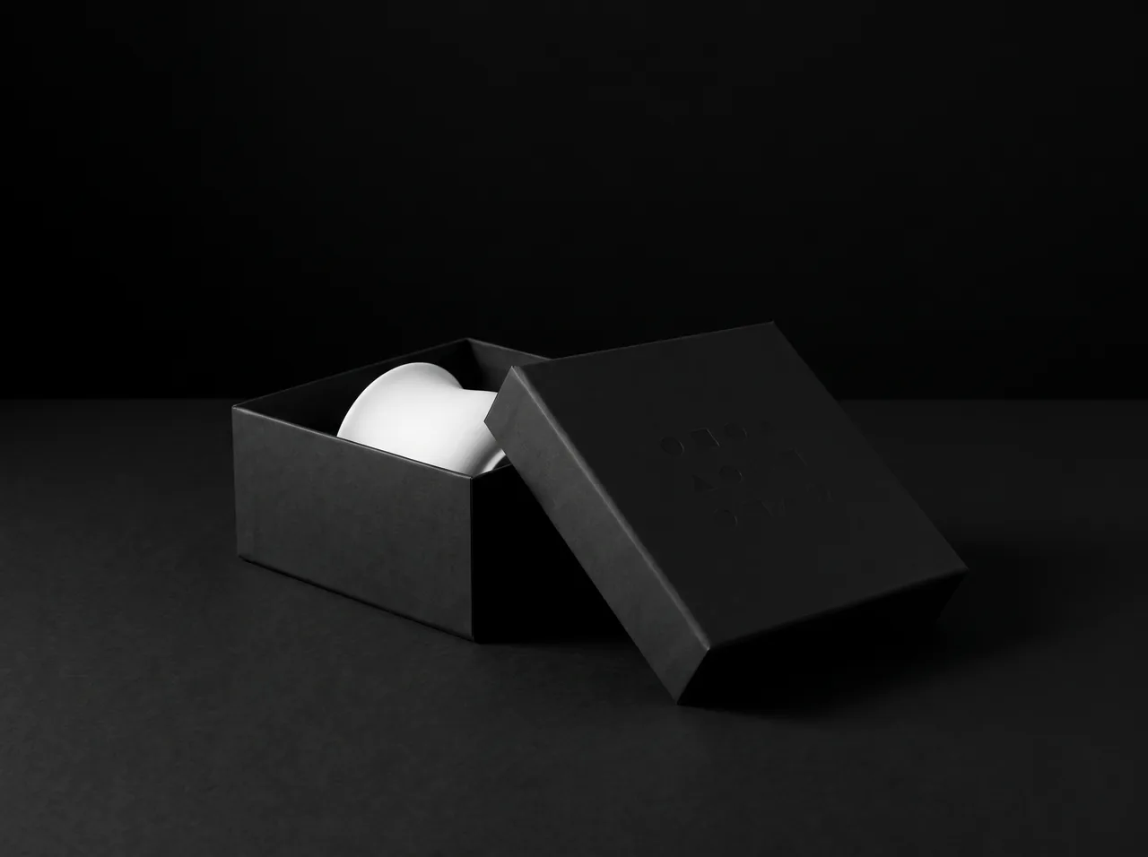 Matte black box with an embossed lid and a porcelain object inside
